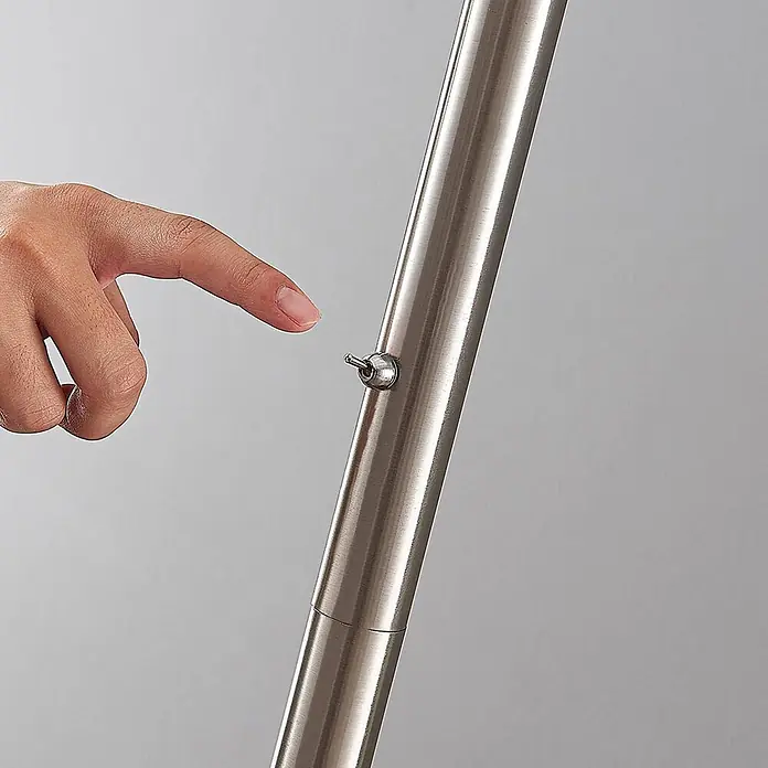 Lindby Stehlampe / Deckenfluter Metall Glas, Standleuchte Nickel satiniert -  - Eine Hand bedient einen kleinen Kippschalter an einem Rohr aus gebürstetem Metall.