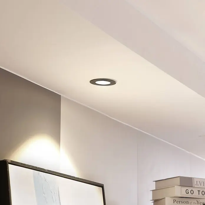 Arcchio Deckenstrahler Lirin - schwarz, schwarz - Einbauspotlight mit schwarzem Ring, in weißer Decke montiert, beleuchtet einen modernen Raum.
