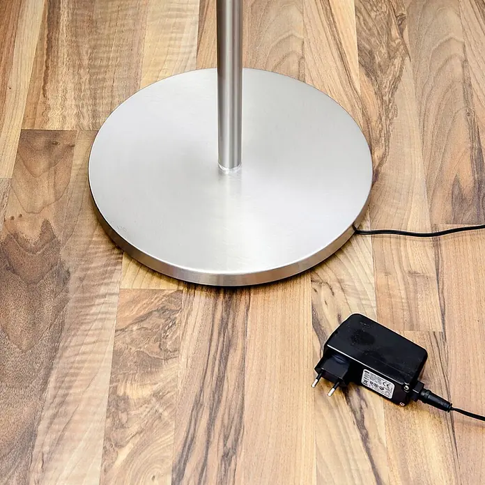Lindby LED Stehlampe, Deckenfluter dimmbar, verstellbarer Lesearm -  - Gebürsteter silberner Lampenfuß mit schwarzem Netzteil und Kabel auf einem Holzboden.