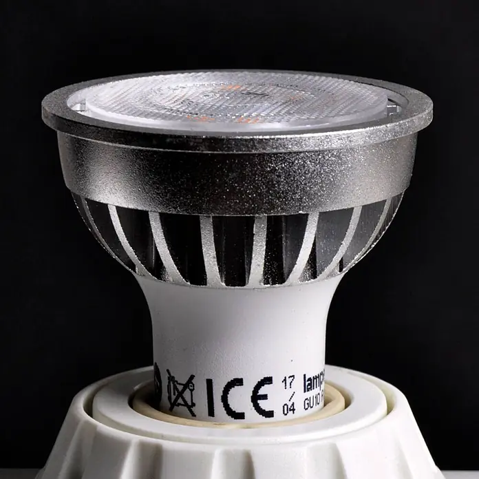 Lindby Leuchtmittel -  - Nahaufnahme einer silbergrauen LED-Spotlampe mit geripptem Kühlkörper und weißem Sockel in einer weißen Fassung.