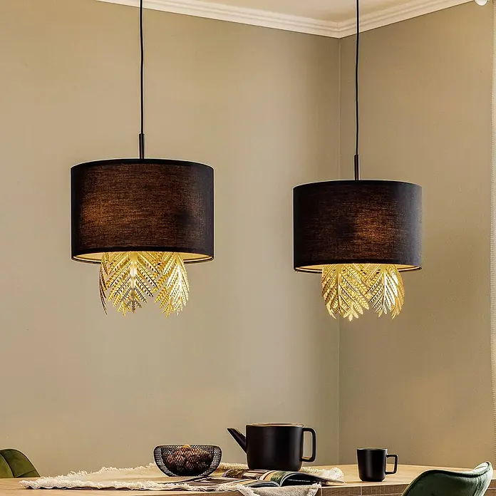 Lucande Pendelleuchte in schwarz, gold, Hängelampe -  - Zwei schwarze Pendelleuchten mit goldenen blattförmigen Dekorelementen, über einem Holzesstisch hängend.