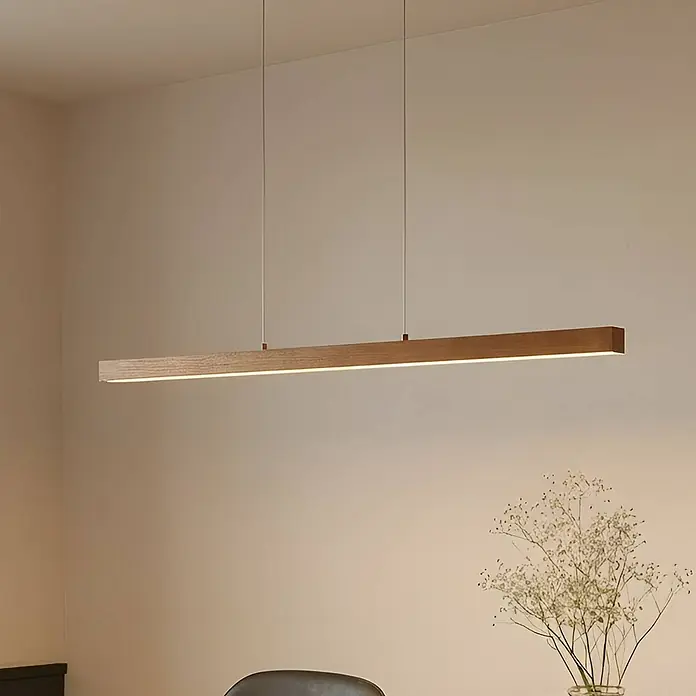 Lucande LED Pendelleuchte in holz, dimmbar Hängelampe -  - Eine lange, lineare Pendelleuchte aus Holz mit integriertem LED-Streifen hängt horizontal und beleuchtet einen Essbereich warm.