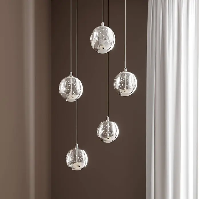 Lucande LED Pendelleuchte in transparent, chrom, Hängelampe -  - Fünf moderne Pendelleuchten mit klaren, sprudelnden Glaskugeln und silberfarbenen Akzenten hängen in einem Raum.