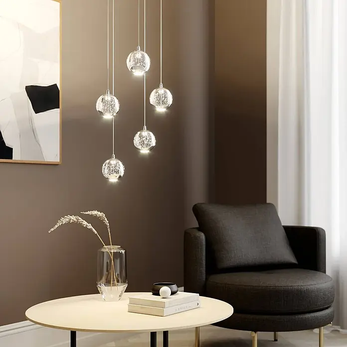 Lucande LED Pendelleuchte in transparent, chrom, Hängelampe -  - Eine Gruppe beleuchteter kugelförmiger Glas-Pendelleuchten mit strukturiertem Inneren hängt in verschiedenen Höhen in einem modernen Wohnzimmer.