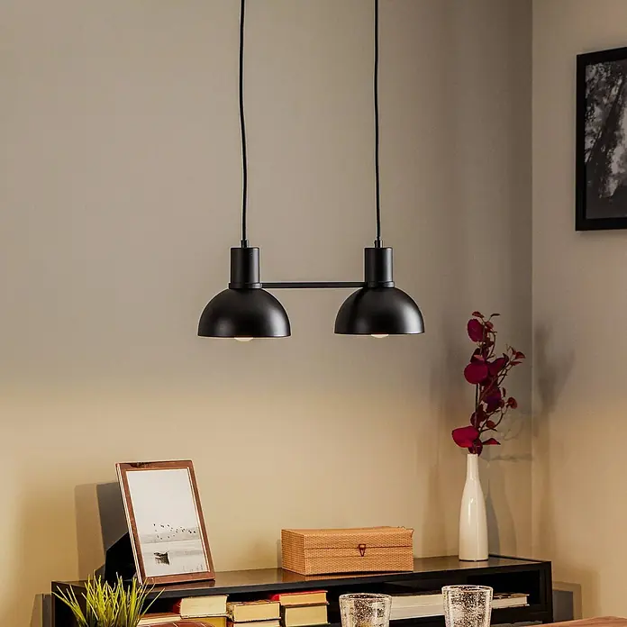 Lucande Pendelleuchte in schwarz matt, Hängelampe -  - Mattschwarze doppelte Pendelleuchte mit zwei gewölbten Schirmen, hängt über einem dunklen Regal mit Deko und beleuchtet den Bereich.