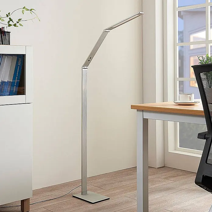 Lucande LED Stehlampe dimmbar, einstellbare Lichtfarbe - 3000-6000K - Verstellbare, silberne LED-Stehleuchte in einem modernen Büro, die einen Arbeitsbereich beleuchtet.