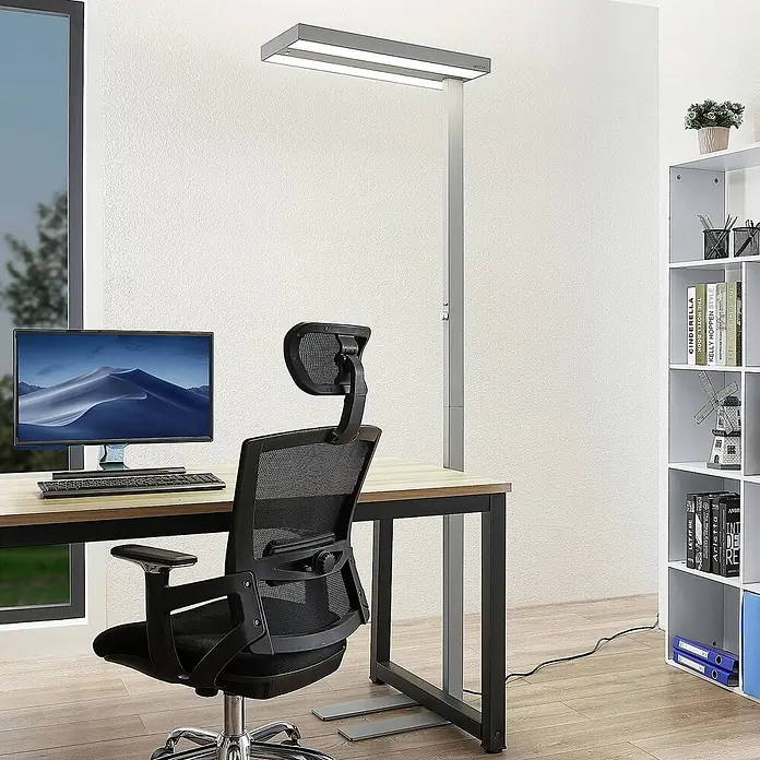 Arcchio LED Büro Stehlampe dimmbar, Bewegungsmelder, Tageslichtsensor -  - Eine moderne, graue ARCCHIO Stehlampe mit rechteckigem Kopf beleuchtet einen Schreibtisch im Home-Office.