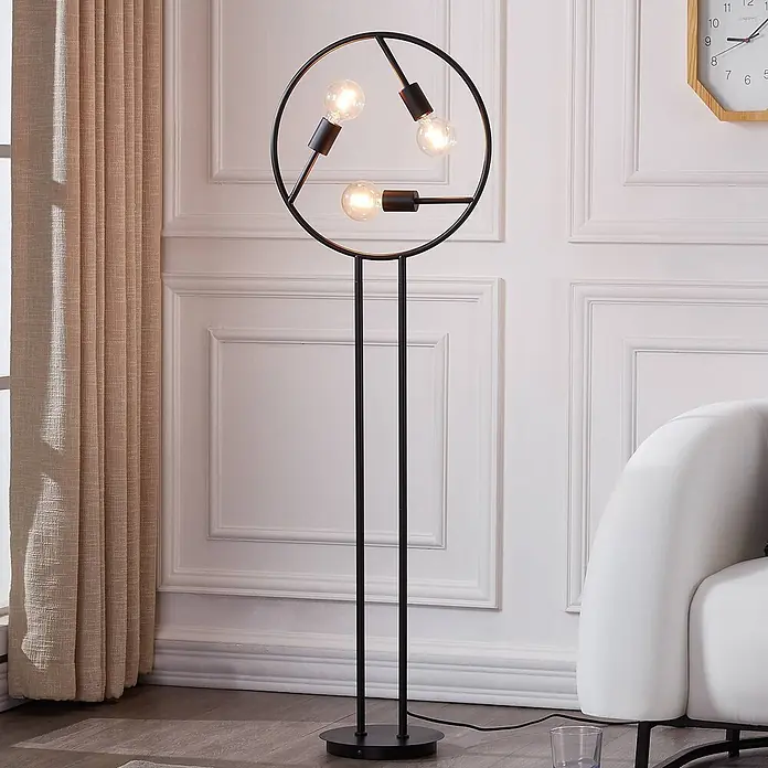 Lucande Stehlampe Wohnzimmer in schwarz, Stehleuchte -  - Eine moderne schwarze Stehlampe aus Metall mit kreisförmigem Kopf und drei sichtbaren Edison-Glühbirnen, die in einem Wohnzimmer neben einem weißen Sofa steht.