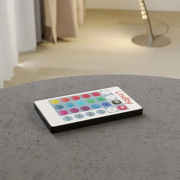 Lindby LED Stehlampe RGB Farbwechsel, dimmbar mit Fernbedienung -  - Weiße Lindby LED-Fernbedienung mit bunten Tasten auf einem grauen Tisch. Sie bietet Power-, Farb- und Modusauswahlen.