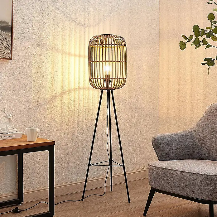 Lindby Stehlampe Wohnzimmer, Tripod in creme, schwarz, Stehleuchte -  - Warm beleuchteter Raum mit einer Stehlampe aus Bambus und schwarzem Metall, die Schatten an die Wand wirft.