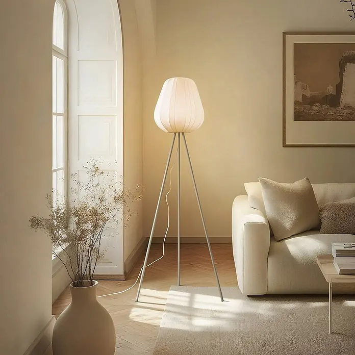 Lindby Stehlampe Wohnzimmer, Tripod in beige, Stehleuchte -  - Eine moderne Dreibein-Stehlampe mit plissiertem cremefarbenem Stoffschirm steht neben einem cremefarbenen Sofa in einem warm beleuchteten Wohnzimmer.