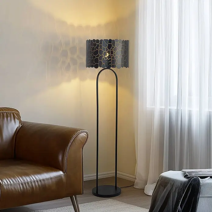 Lindby Stehlampe Wohnzimmer in schwarz, gold, Stehleuchte -  - Schwarze Stehlampe mit geometrischem gold-schwarzem Musterschirm, die ein modernes Wohnzimmer neben einem braunen Ledersofa beleuchtet.