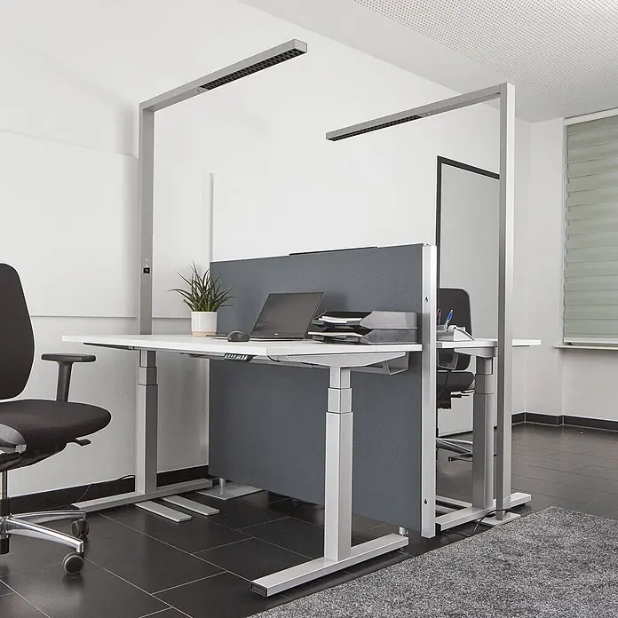 Arcchio LED Büro Stehlampe dimmbar, Bewegungsmelder, Tageslichtsensor -  - Zwei silber-graue höhenverstellbare Bürotische mit weißen Platten, integrierter Deckenbeleuchtung und grauen Sichtschutzwänden im Büro.