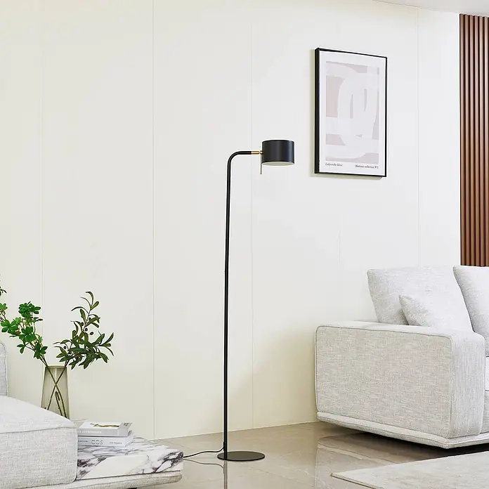 Lindby Stehlampe Wohnzimmer in schwarz, Stehleuchte -  - Elegante schwarze Stehlampe mit zylindrischem Kopf und Messingakzent, neben einem hellen Sofa in einem modernen Wohnzimmer stehend.