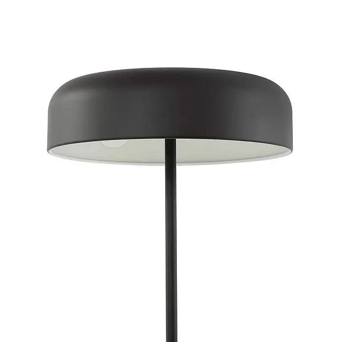 Lindby Stehlampe Wohnzimmer in schwarz, Stehleuchte -  - Nahaufnahme eines modernen, mattschwarzen Lampenschirms mit weißer Innenseite, gestützt von einer schlanken dunklen Stange.