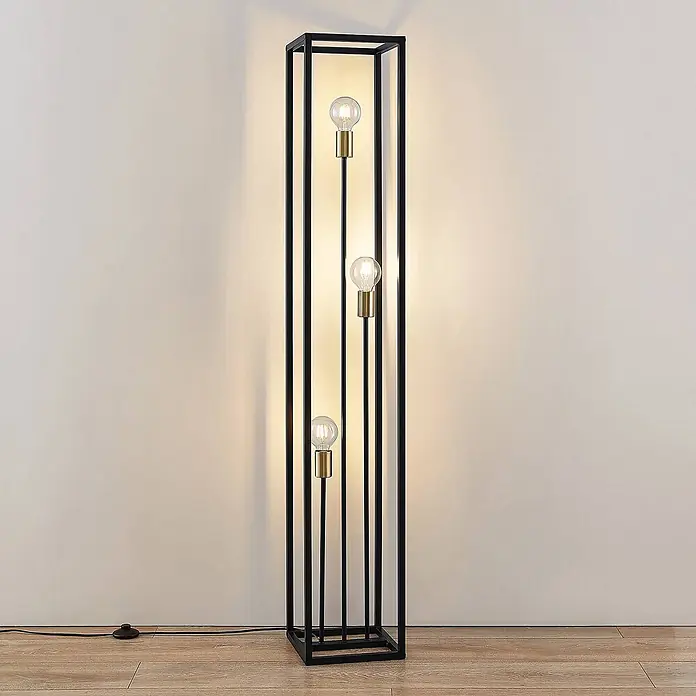 Lindby Stehlampe Wohnzimmer in schwarz matt, Stehleuchte -  - Schlanke schwarze Metall-Stehleuchte mit drei sichtbaren Glühbirnen mit Messingsockel, auf Holzfußboden.