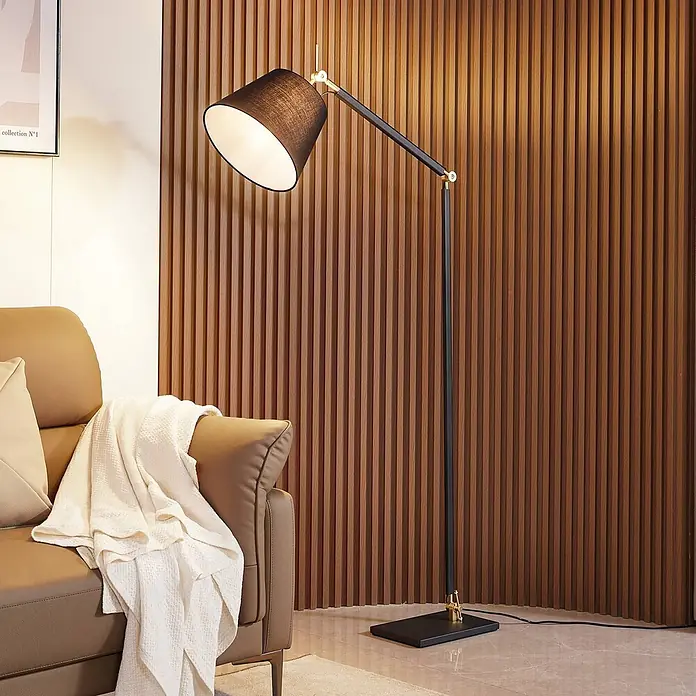 Lucande Stehleuchte Marvaine - schwarz, schwarz, E27 - Schwarze, verstellbare Stehlampe mit Stoffschirm und goldenen Akzenten, beleuchtet einen Wohnbereich neben einem braunen Sofa.