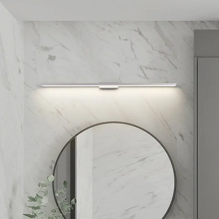 Lindby Wandleuchte Alenia - alu / grau / zink - Schlanke silberne LED-Spiegelleuchte horizontal über einem runden Badspiegel montiert, spendet helles Licht.