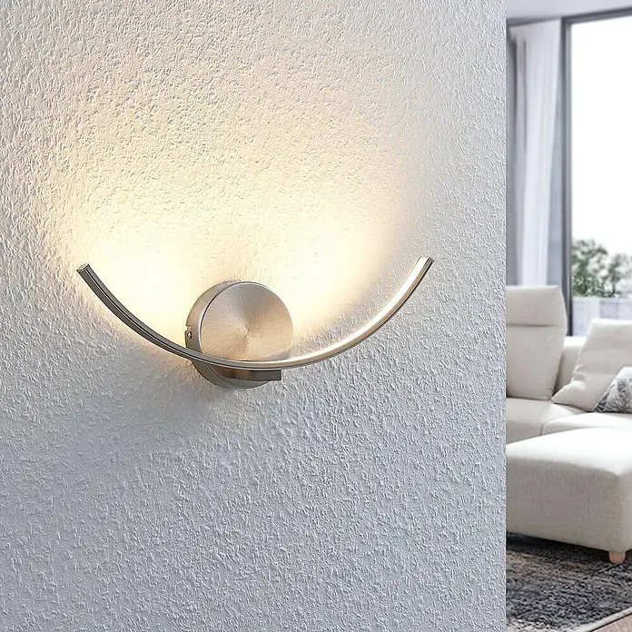 Lindby LED Wandleuchte innen in nickel satiniert, weiß Wandfluter -  - Moderne geschwungene LED-Wandleuchte aus gebürstetem Metall, die warmes Licht auf eine strukturierte Wand wirft.