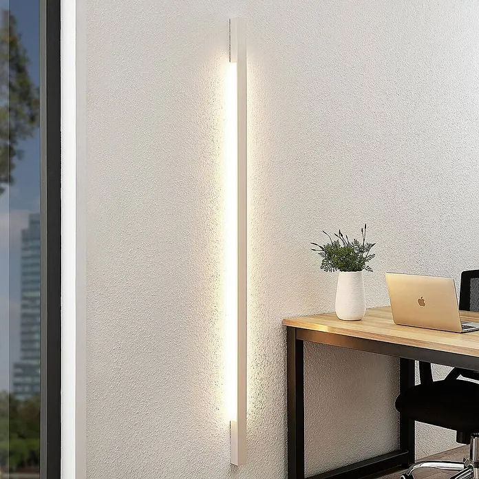 Arcchio LED Wandleuchte innen in weiß, Wandlampe -  - Eine lange, weiße LED-Wandleuchte, vertikal montiert, spendet warmes, indirektes Licht in einem modernen Büro.