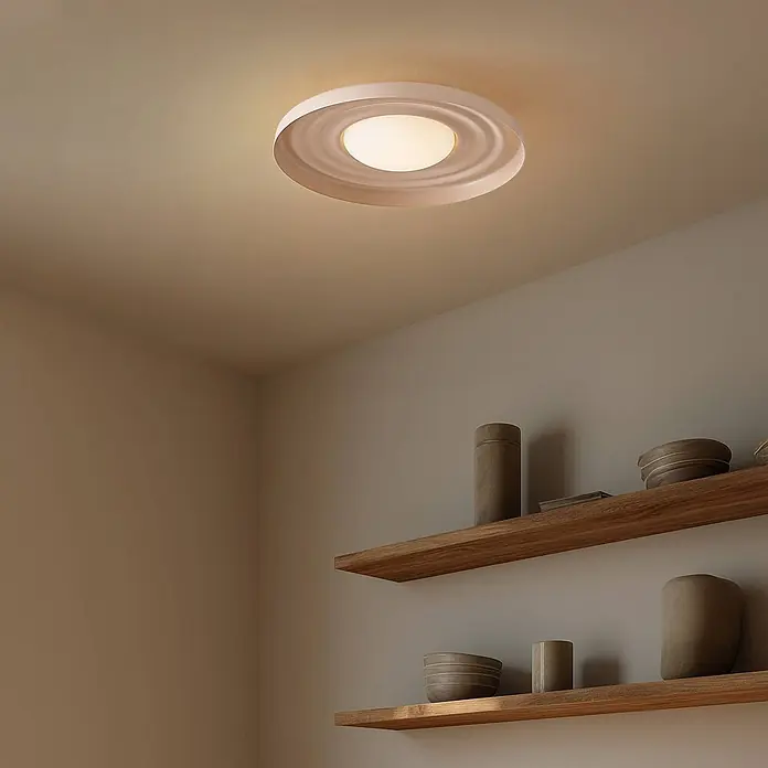 Lindby Wandleuchte Waves - creme / amber - Runde, helle Deckenleuchte beleuchtet einen Raum mit Holzregalen.
