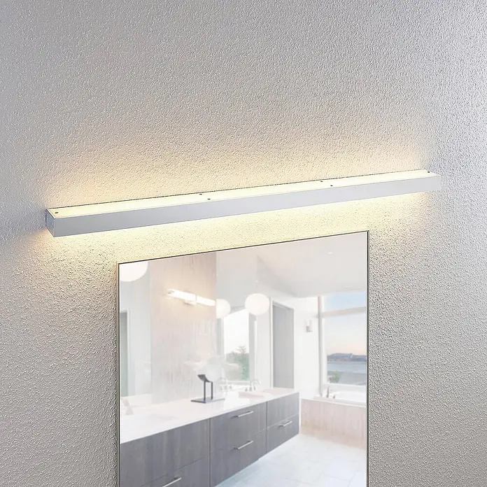Lindby LED Wandleuchte innen in chrom, weiß, up down Wandlampe -  - Eine schlanke weiße lineare LED-Leuchte ist über einem Spiegel montiert und beleuchtet einen modernen Badezimmerwaschtisch.