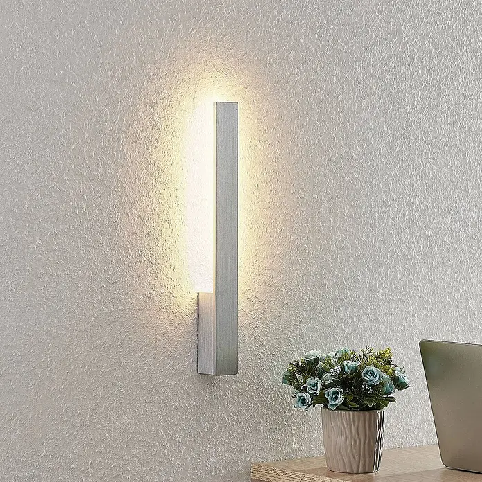 Arcchio LED Wandleuchte innen in aluminium gebürstet, Wandlampe -  - Moderne Wandleuchte aus gebürstetem Aluminium an einer strukturierten Wand, die warmes Licht nach oben und unten wirft.