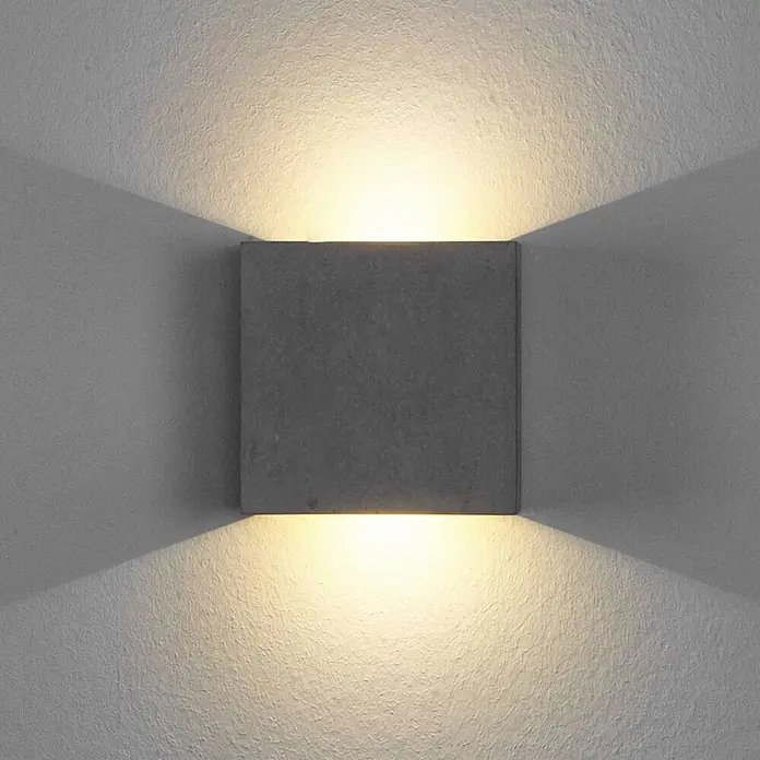Lindby Wandleuchte Yva - alu / grau / zink - Quadratische, dunkelgraue Wandleuchte für Up-Down-Beleuchtung, beleuchtet eine strukturierte Wand mit warmem Licht.