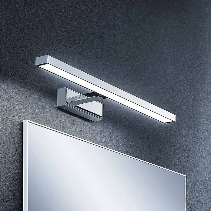 Lindby LED Wandleuchte innen in weiß, chrom, Wandlampe -  - Moderne Chrom-LED-Spiegelleuchte an dunkler Wand über einem rechteckigen Spiegel.