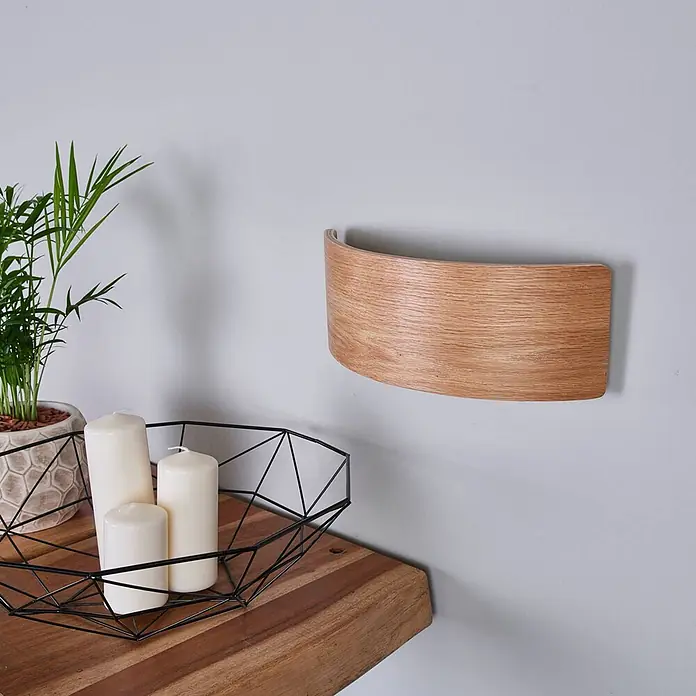 Lindby LED Holz Wandlampe 33 cm, Wandleuchte innen Uplight and Downlight -  - Eine gebogene Holz-Wandleuchte, die stimmungsvolles Licht über einem Holzregal mit Pflanze und Kerzen spendet.