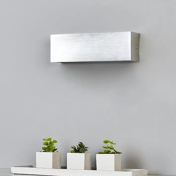 Lindby Wandleuchte Ranik - alu / grau / zink, alu / grau / zink - Silberne rechteckige Wandleuchte an einer Wand über drei kleinen Topfpflanzen.