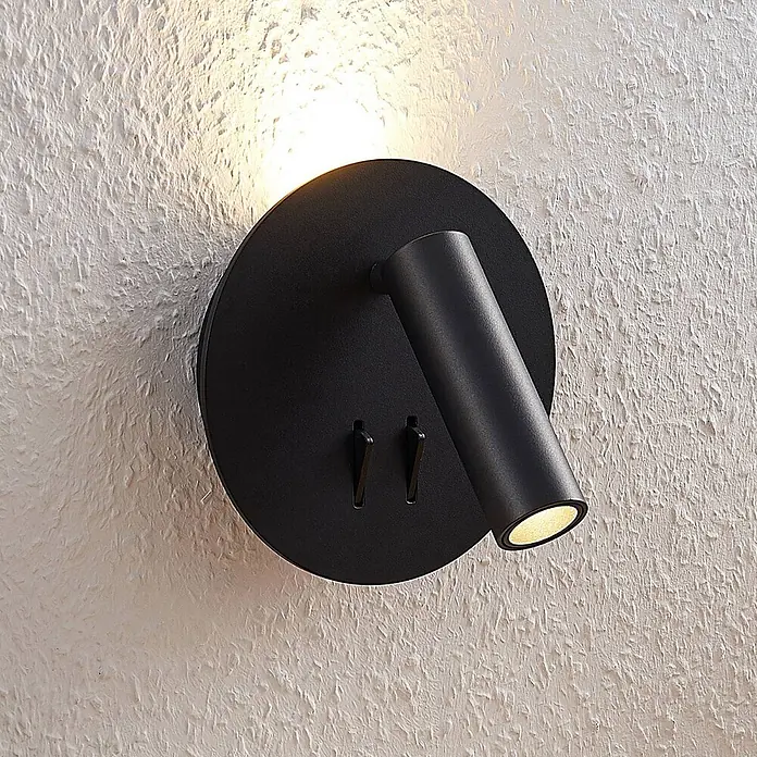 Lucande LED Wandleuchte innen in schwarz matt, Wandlampe -  - Mattschwarze Wandleuchte mit verstellbarem Strahler und zwei kleinen Hebeln, die eine strukturierte weiße Wand beleuchtet.