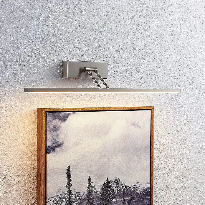 Lucande Wandleuchte Thibaud - alu / grau / zink - Satinierte Nickel-LED-Bilderleuchte beleuchtet ein gerahmtes Kunstwerk.