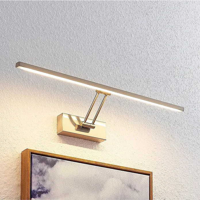 Lucande Wandleuchte Thibaud - alu / grau / zink - Gebürstete Messing LED-Bilderleuchte mit verstellbarem Arm, die ein gerahmtes Kunstwerk beleuchtet.