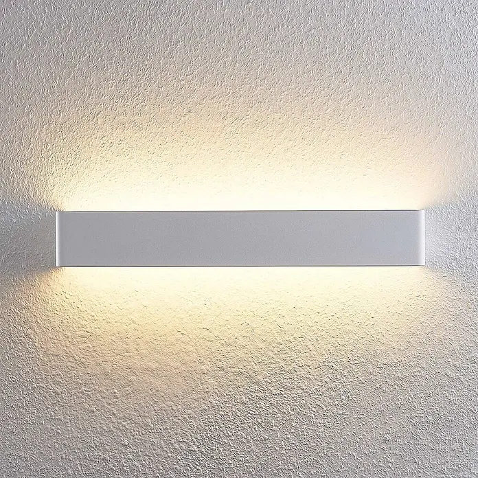 Arcchio LED Wandleuchte innen in weiß, Wandlampe -  - Eine moderne, graue lineare Wandleuchte strahlt warmweißes Licht nach oben und unten an einer strukturierten Wand ab.