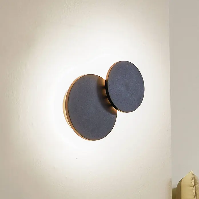 Lucande Wandleuchte Elrik - schwarz - Moderne Wandleuchte mit zwei überlappenden dunkelgrauen Kreisscheiben und goldenem Rand, die ein warmes Licht abgibt.