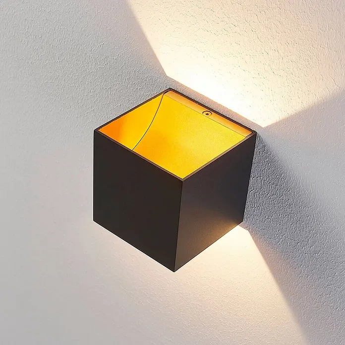 Arcchio LED Wandleuchte innen in schwarz, orange, Wandlampe -  - Dunkle kubische Wandleuchte mit goldenem Inneren, die Licht nach oben und unten auf eine texturierte Wand abgibt.