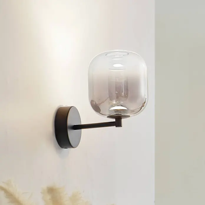 Lucande Wandleuchte Avelina - schwarz, alu / grau / zink - Moderne Wandleuchte mit rundem schwarzem Sockel, horizontalem Arm und klarem Rauchglas-abgerundetem Schirm.