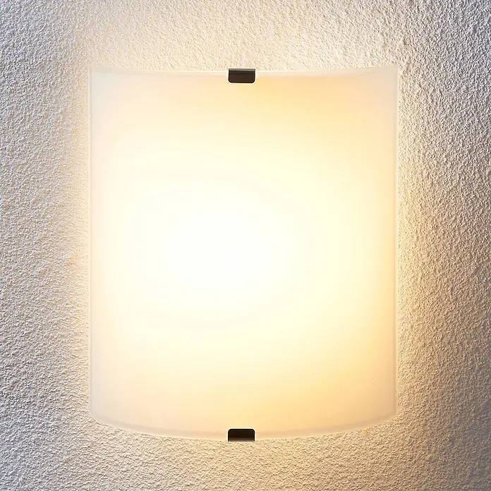 Lindby LED Wandleuchte innen in transparent satiniert, Wandlampe -  - Warm leuchtende Wandleuchte aus satiniertem Glas, an einer strukturierten Wand mit dunklen Metallklammern montiert.