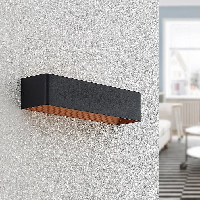 Arcchio LED Wandleuchte innen in schwarz, gold, Wandlampe -  - Rechteckige schwarze Wandleuchte mit kupferfarbener Innenseite, an einer strukturierten weißen Wand montiert, für Akzentbeleuchtung.