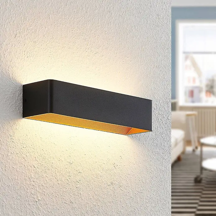 Arcchio LED Wandleuchte innen in schwarz, gold, Wandlampe -  - Rechteckige schwarze Wandleuchte mit goldener Innenseite, an einer strukturierten Wand montiert, die warmes Licht abstrahlt.