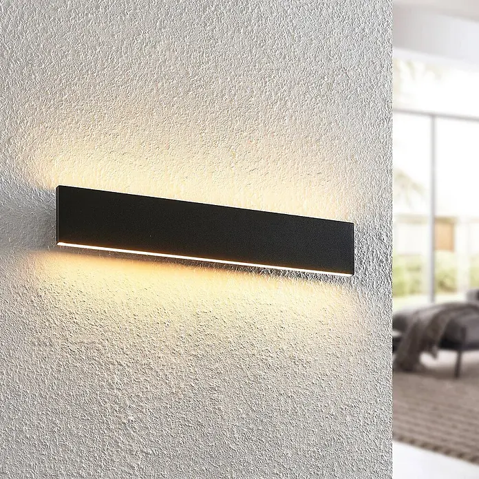 Lindby LED Wandleuchte innen in schwarz, up down Wandlampe -  - Schwarze, rechteckige LED-Wandleuchte strahlt warmes Licht auf eine strukturierte Wand.
