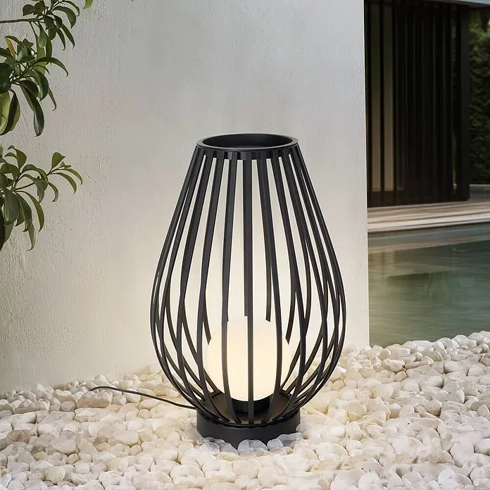 Lucande Außenstehleuchte Marrin -  - Schwarze Outdoor-Lampe mit Metallgitter und weißer Kugelleuchte, auf weißen Kieselsteinen an einer Wand und Pool.