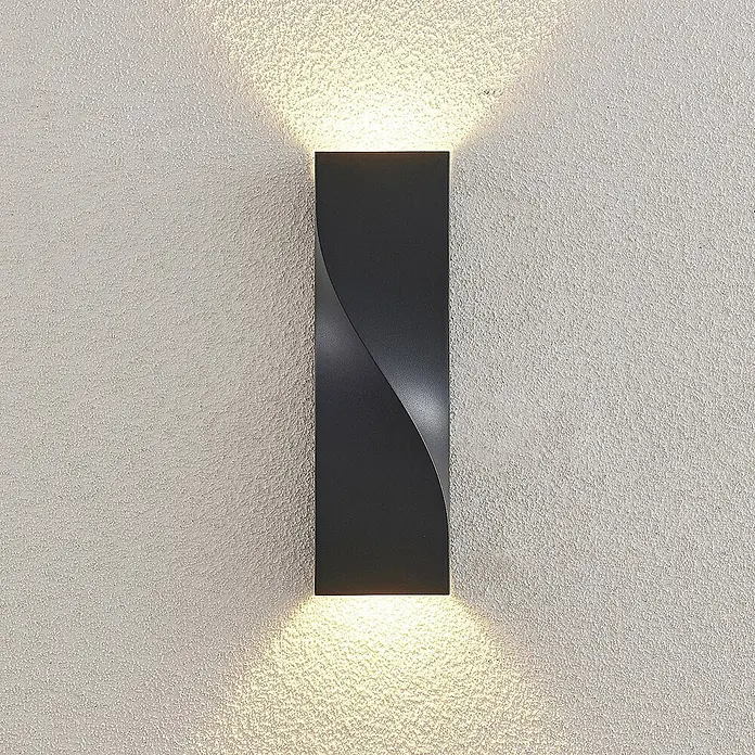 Lucande LED Wandleuchte aussen in anthrazit, Aussenlampe Wand -  - Schwarze rechteckige Wandleuchte mit verdrehter Front, die warmes Licht nach oben und unten auf eine strukturierte Wand wirft.