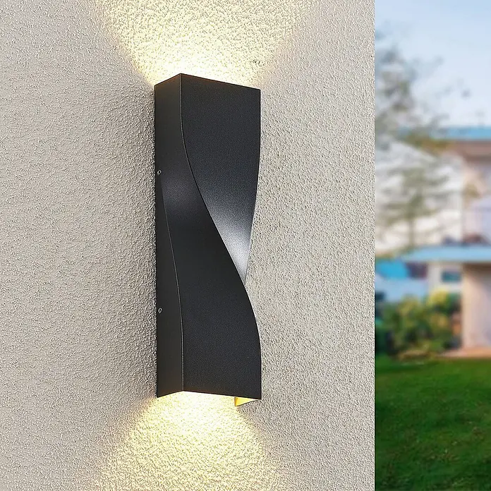 Lucande LED Wandleuchte aussen in anthrazit, Aussenlampe Wand -  - Schwarze, verdrehte Außenwandleuchte an einer strukturierten Wand, die warmes Licht nach oben und unten wirft.