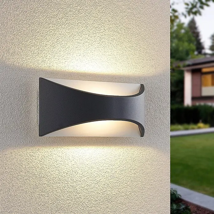 Lindby LED Wandleuchte aussen in anthrazit, weiß, Aussenlampe Wand -  - Moderne dunkelgraue Außenwandleuchte, die warmes Licht nach oben und unten abstrahlt, an einer strukturierten Wand montiert.