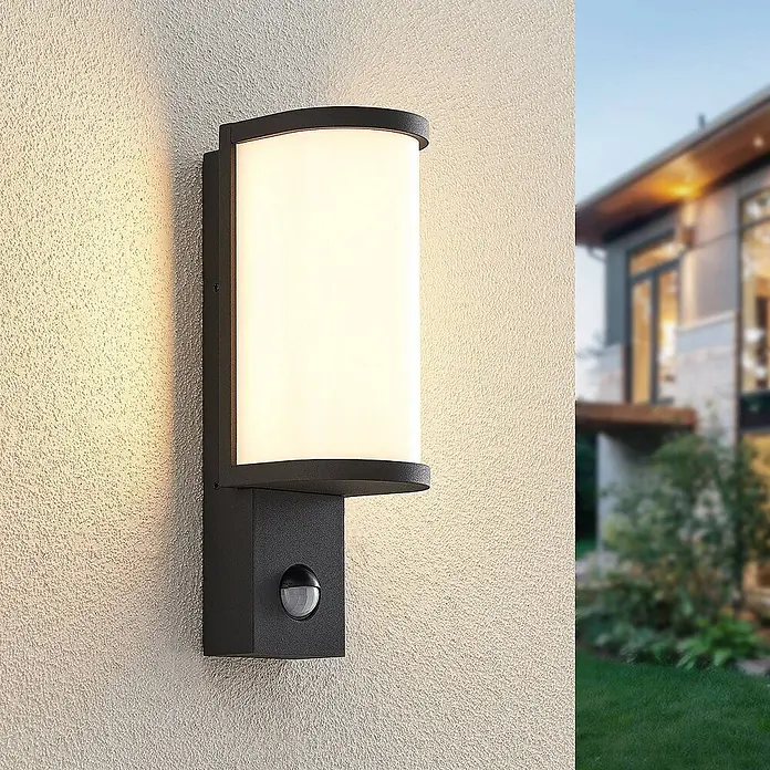 Lucande LED Wandleuchte aussen in graphit, weiß, mit Bewegungsmelder, -  - Schwarze Außenwandleuchte mit weißem Lichtpaneel und Bewegungsmelder, an einer Hauswand montiert.