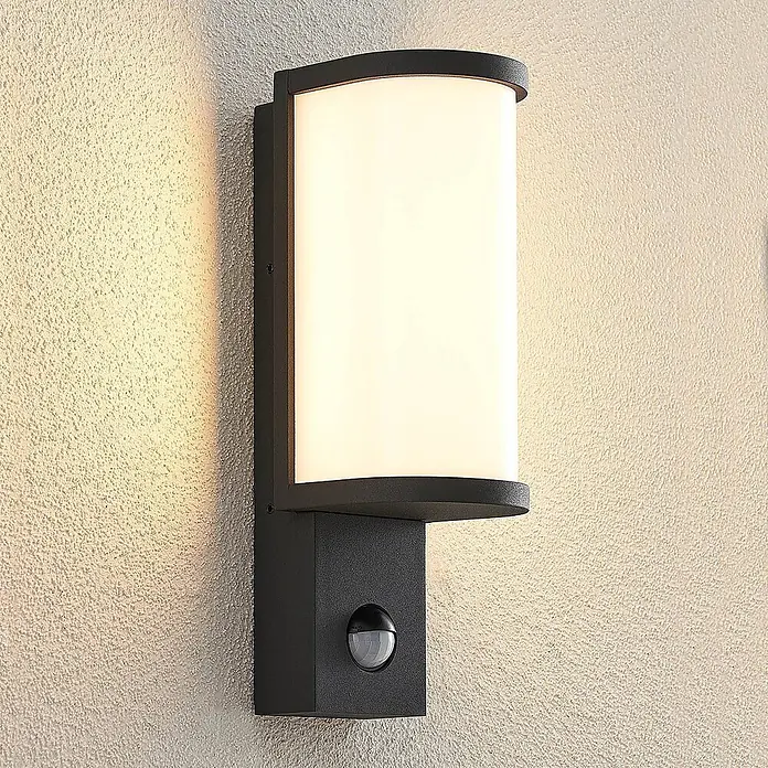 Lucande LED Wandleuchte aussen in graphit, weiß, mit Bewegungsmelder, -  - Schwarze Außenwandleuchte mit gebogenem Diffusor und Bewegungssensor an einer hellen, strukturierten Wand.