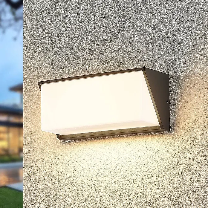 Lindby LED Wandleuchte aussen in anthrazit, weiß, Aussenlampe Wand -  - Rechteckige dunkle Metall-Außenwandleuchte mit weißem Diffusor, die eine strukturierte Wand darunter beleuchtet.