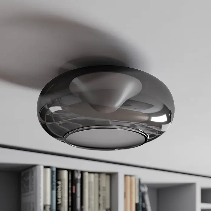 Lucande Deckenleuchte Mijo - alu / grau / zink - Runde Deckenleuchte aus Rauchglas mit konischem Diffusor, über einem Bücherregal montiert.